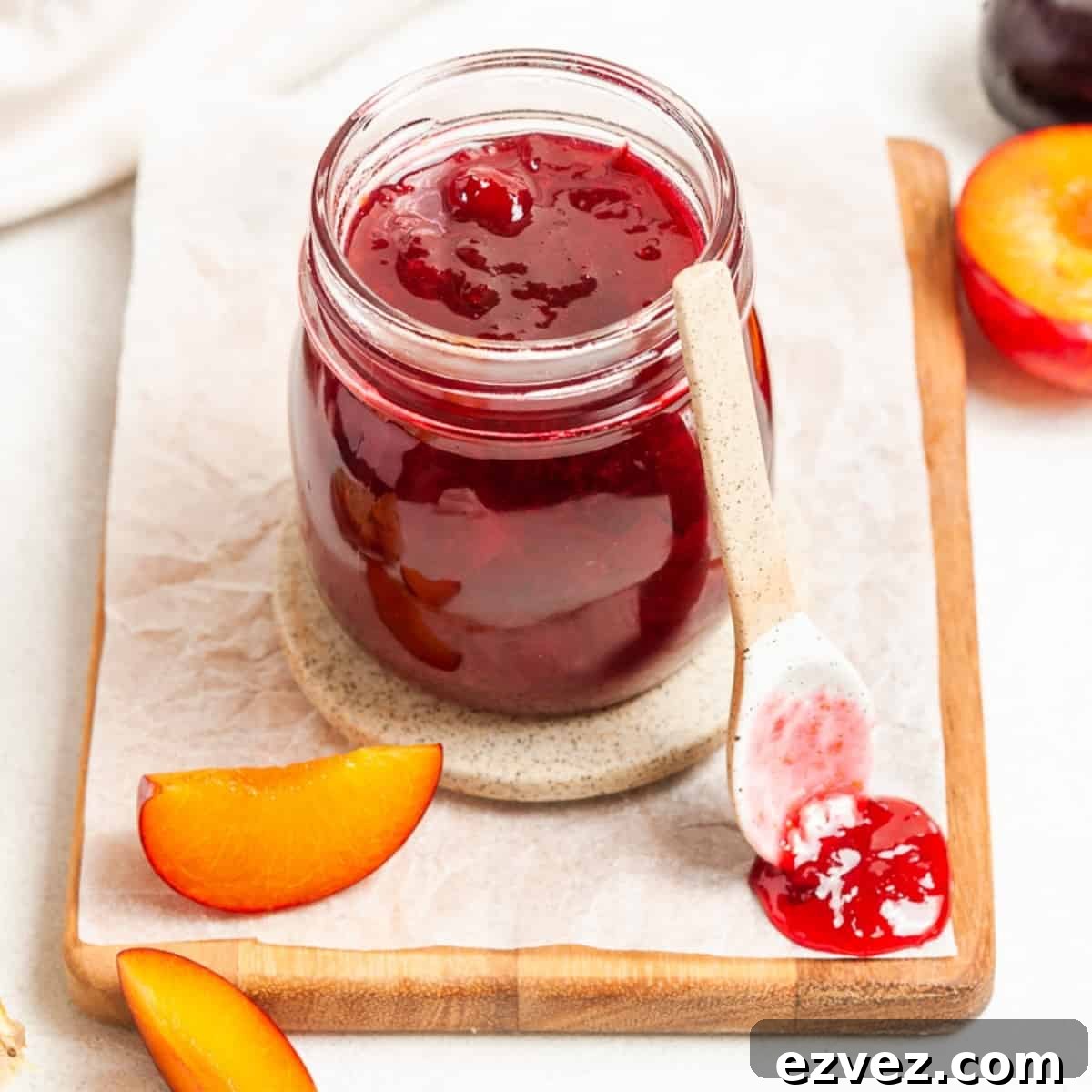 Jar of jam, sitting on a board, with a spoon and a dollop of jam on the edge.