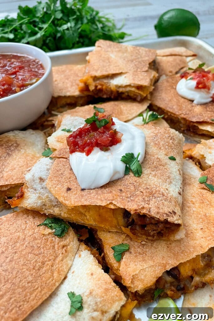 sheet pan quesadillas cut into individual squares topped with sour cream, salsa, and cilantro