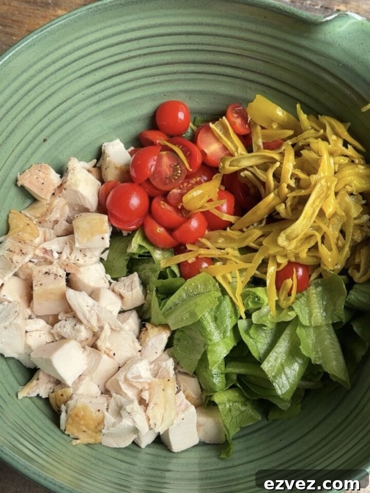 a photo of lettuce, chicken, tomatoes and pepperoncini in a bowl