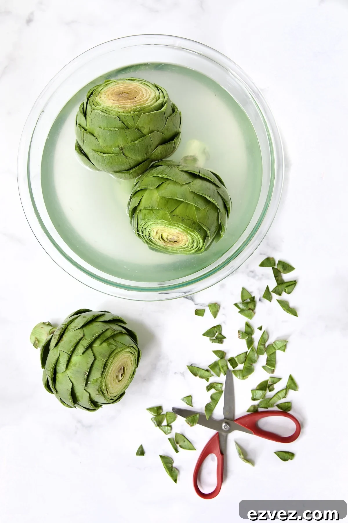 Three artichokes being trimmed with two in lemon water.