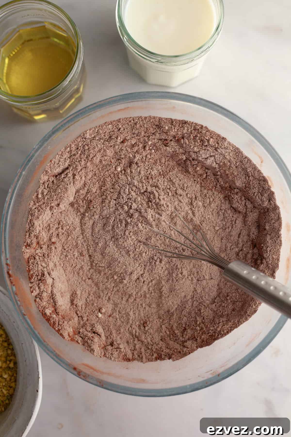 A bowl with a whisk and flour and cocoa powder.
