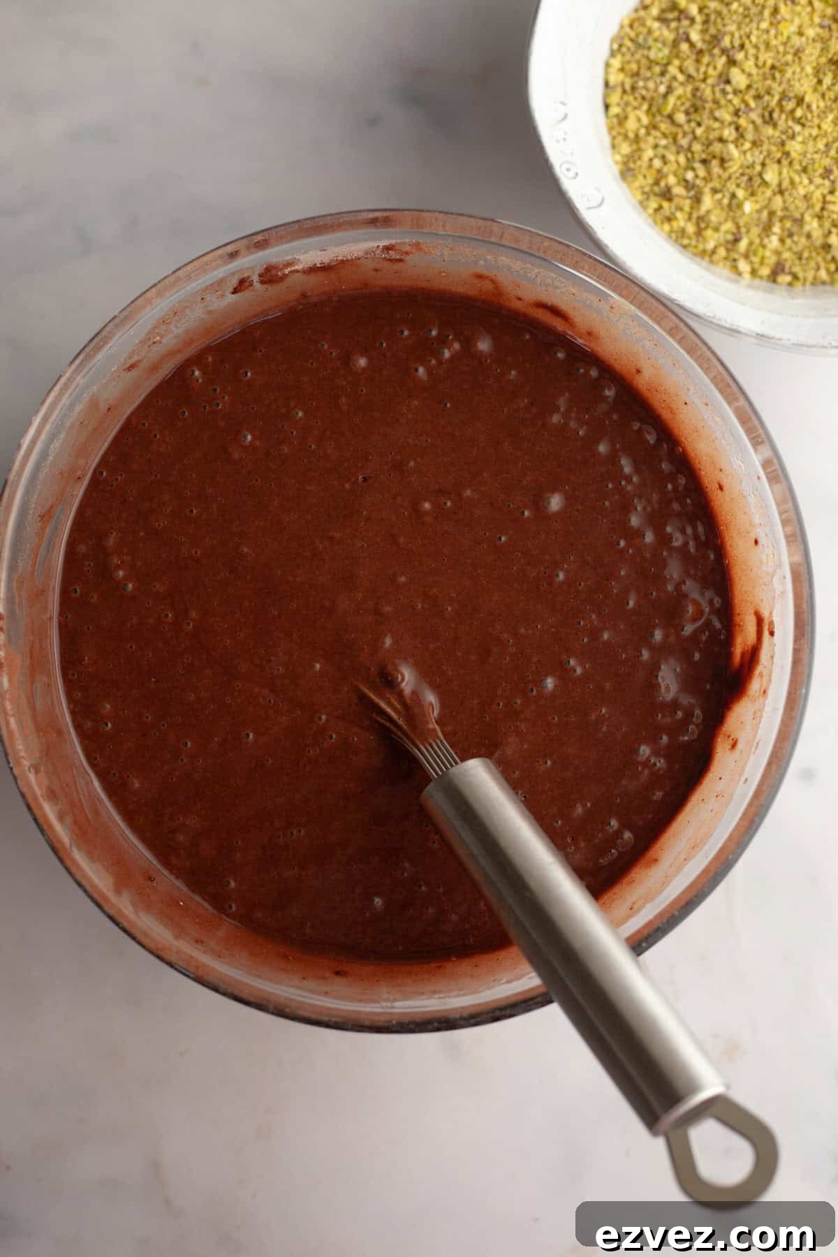 Chocolate cake batter with a silver whisk in a glass bowl.