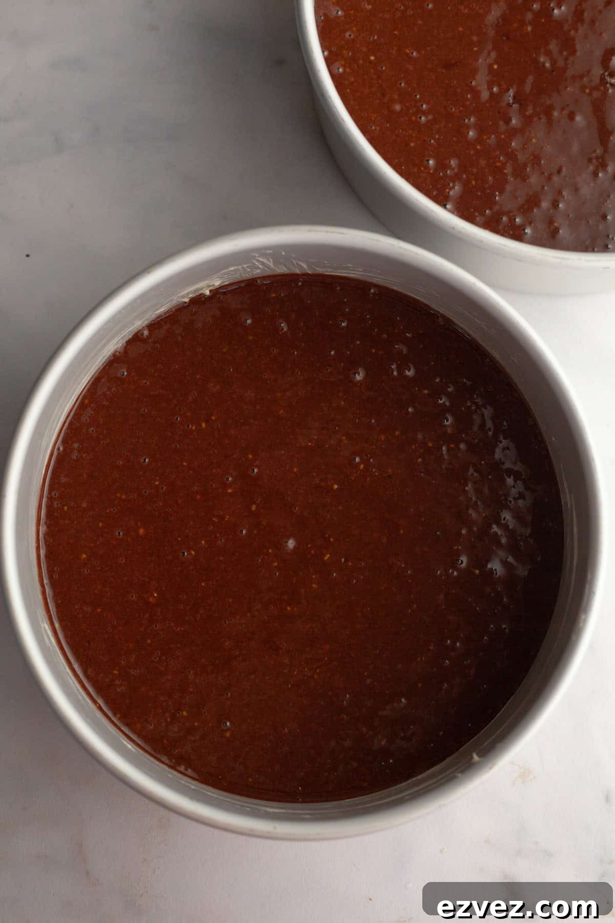 Two round cake pans with unbaked chocolate cake batter.