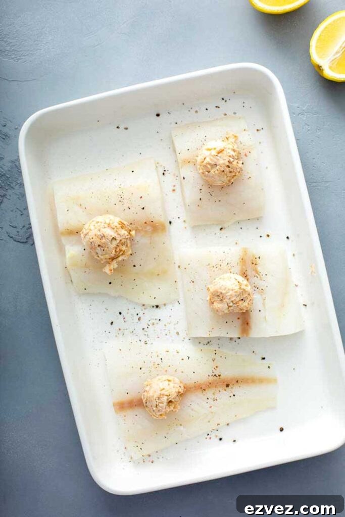 Uncooked fillets of cod fish topped with Cajun butter in a baking dish ready to be cooked in the oven