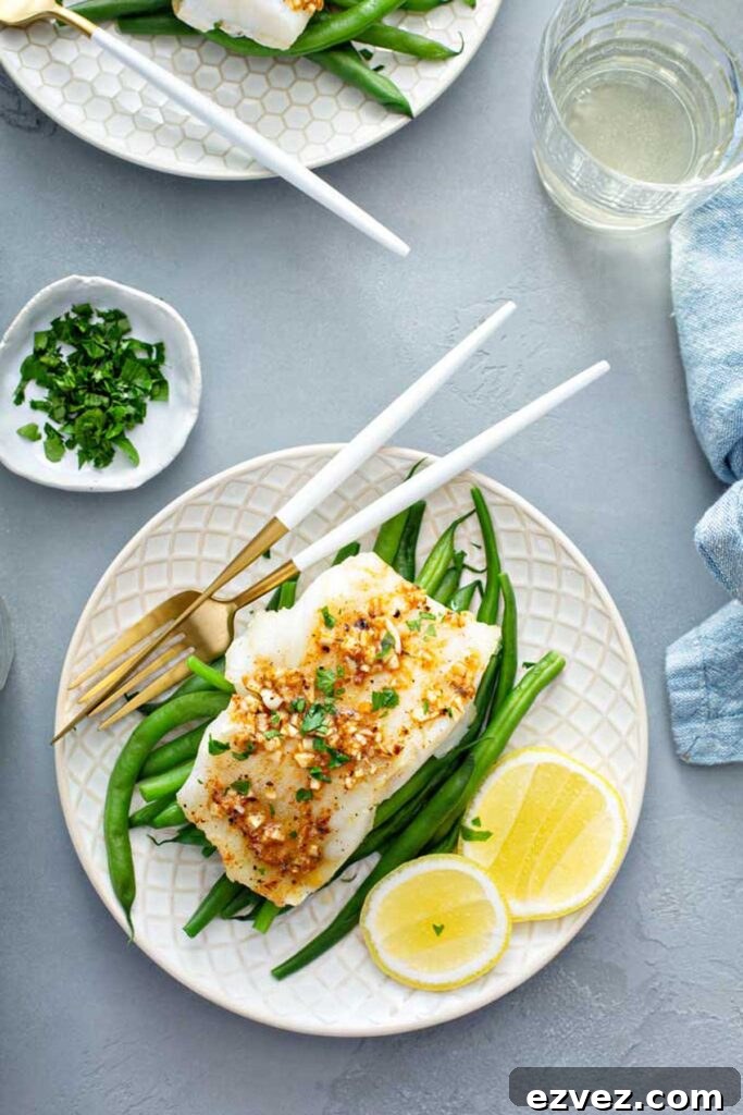 A plate with a fillet of baked cod over green beans topped with Cajun butter