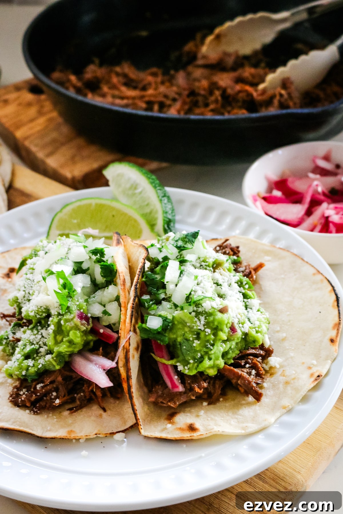 Slow-Cooker Shredded Beef Tacos for Flavorful Weeknight Meals 5 Roast tacos on a white plate with roasted beef in a pan beside them.
