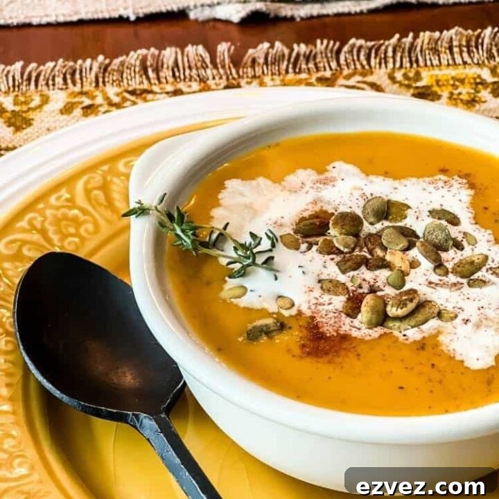 Bowl of dairy free autumn squash soup garnished with coconut milk and pumpkin seeds on a plate with a black metal spoon