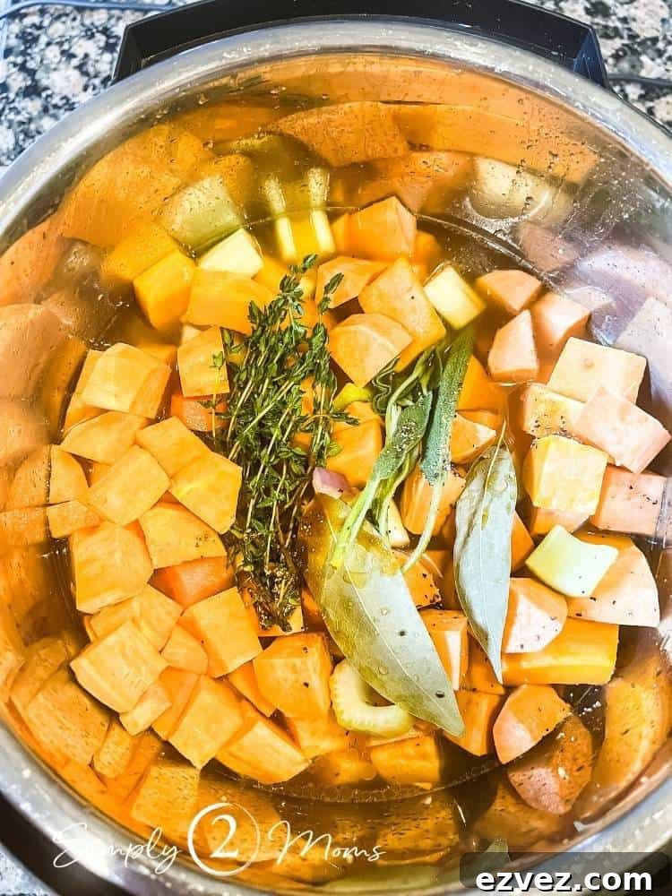 Instant pot filled with chopped butternut squash, onions, sweet potatoes, carrots, celery, and fresh herbs