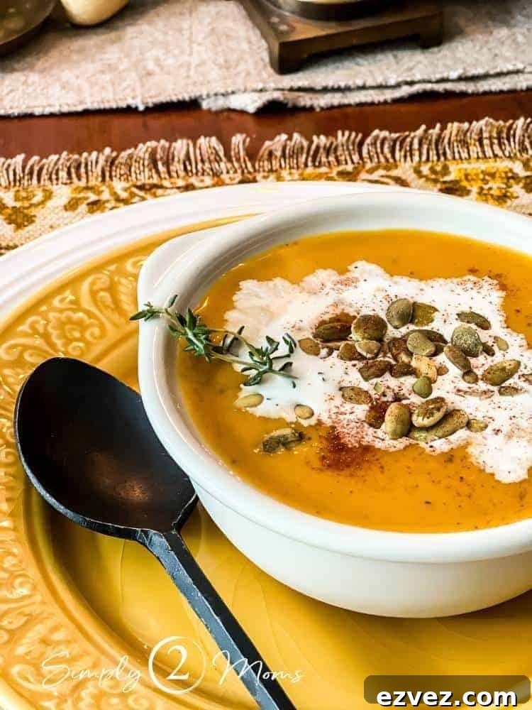 Bowl of dairy free autumn squash soup garnished with coconut milk and pumpkin seeds on a plate with a black metal spoon