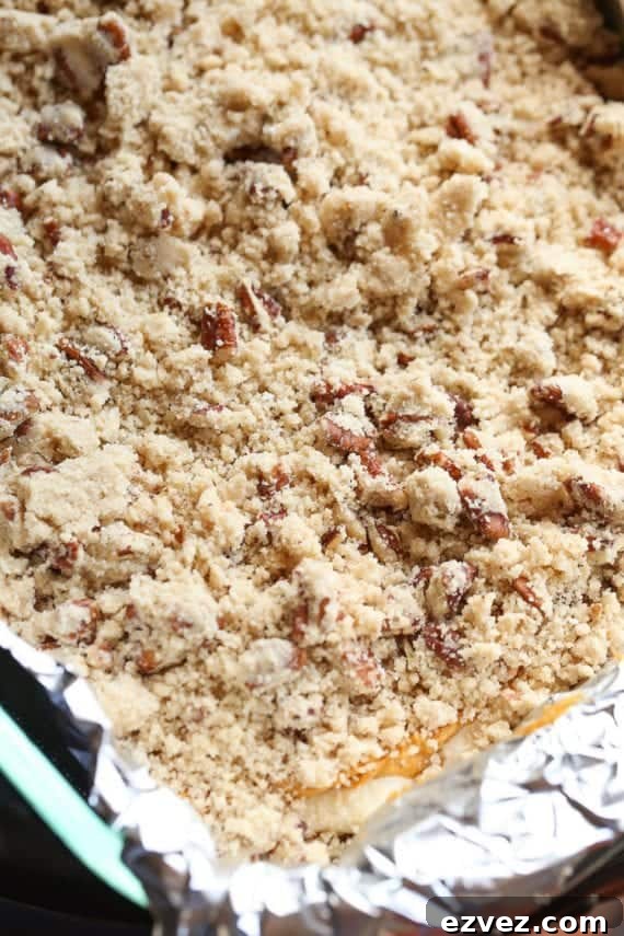 Unbaked pumpkin cheesecake bars topped with praline in a lined baking pan.
