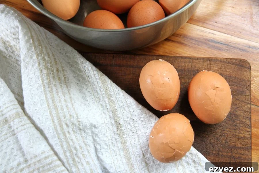 The boiled eggs with mashed shells sitting on a cutting board next to a stainless steel pot of eggs