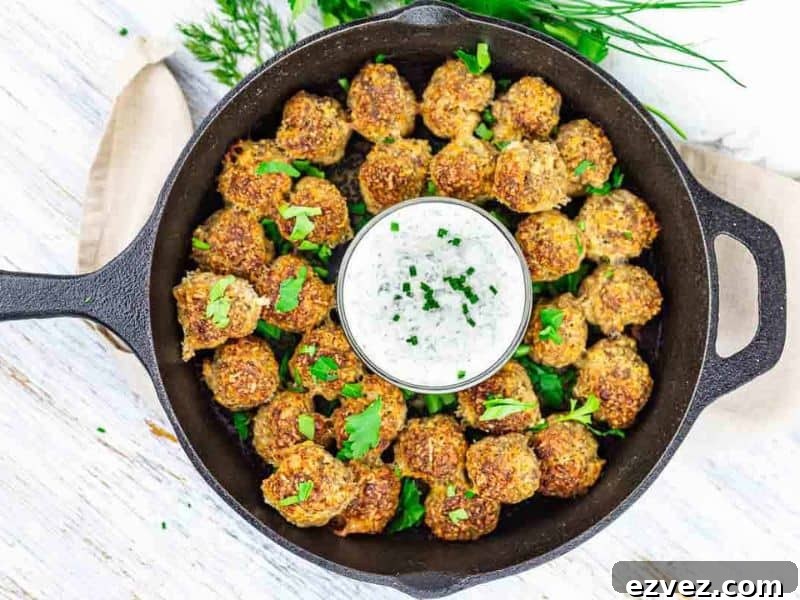 11 Party Appetizers Guests Devour Immediately 13 A cast iron skillet filled with cooked meatballs garnished with herbs, arranged around a bowl of white dipping sauce topped with chopped chives.