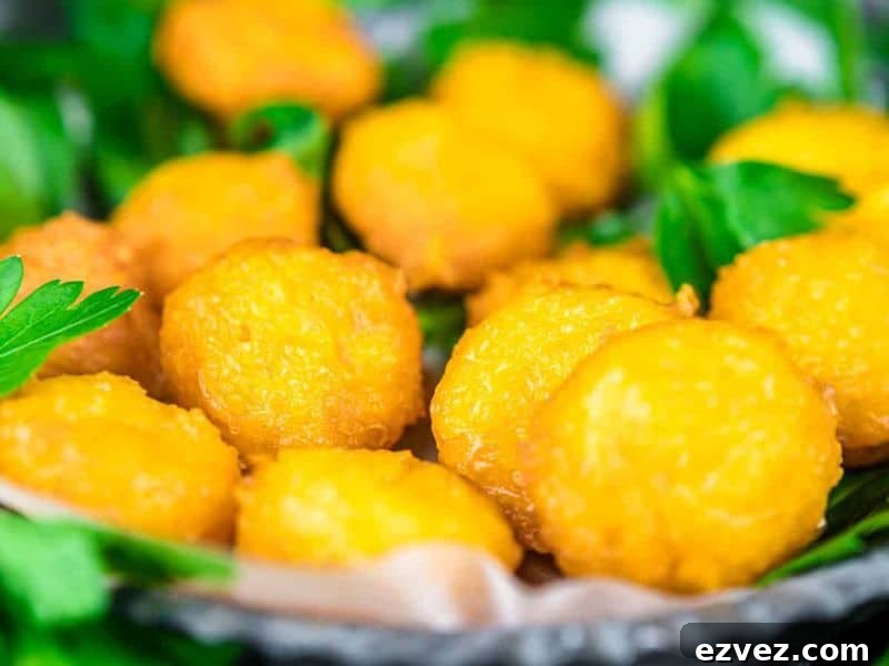 11 Party Appetizers Guests Devour Immediately 5 Close-up of several golden-brown fried cheese balls on a tray, garnished with fresh green parsley leaves.