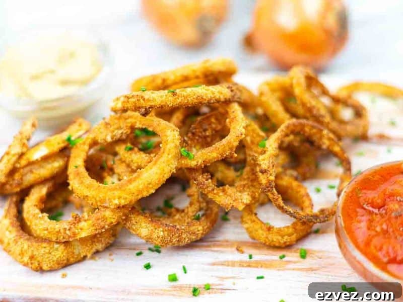 11 Party Appetizers Guests Devour Immediately 6 A pile of crispy breaded onion rings garnished with chopped chives on a wooden board, served with bowls of ketchup and mustard sauce.