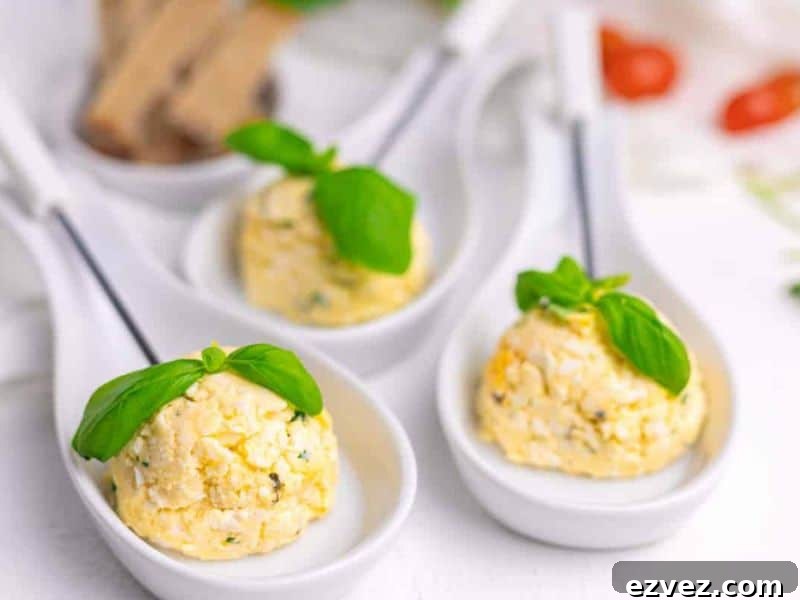 11 Party Appetizers Guests Devour Immediately 7 Three white ceramic spoons each hold a scoop of herbed cheese or spread, garnished with a fresh basil leaf, arranged on a white surface.