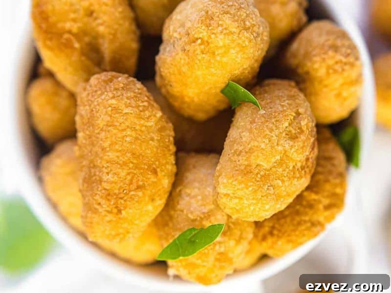 11 Party Appetizers Guests Devour Immediately 8 A white bowl filled with golden-brown, crispy, breaded nuggets garnished with a few small green leaves.