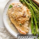 Small white plate with a tender pan-fried chicken breast in white wine sauce, roasted asparagus, and a slice of bread.