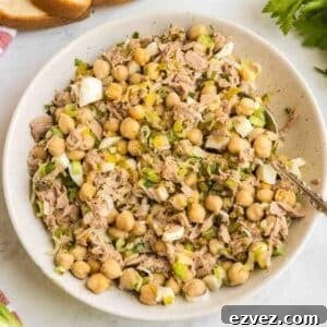 A bowl of chickpea tuna salad with chopped green onions and celery, mixed together and served with a spoon.