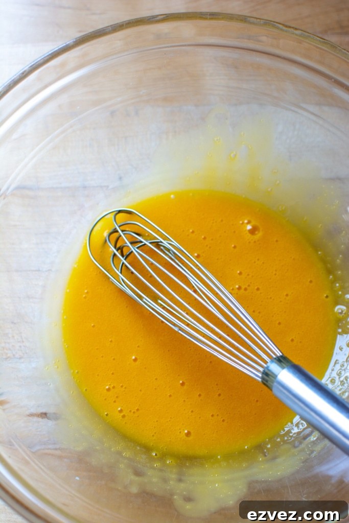Egg yolks with a whisk in a glass bowl.