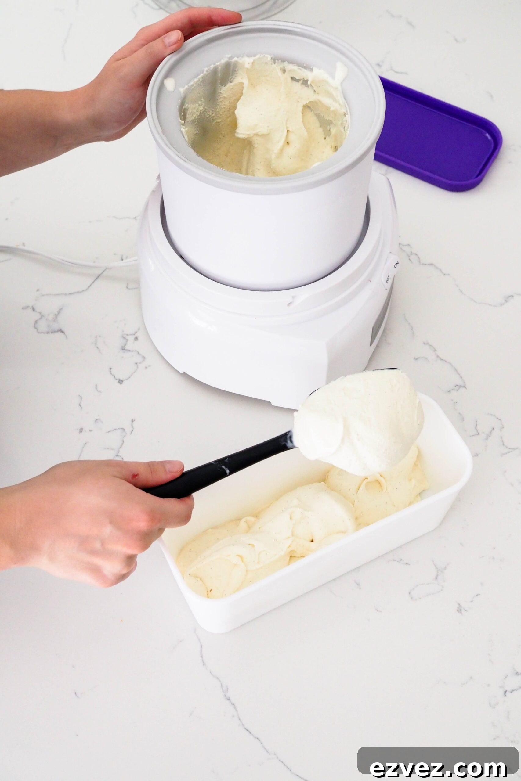 A hand scoops ice cream out of an ice cream maker canister and into a rectangular container.