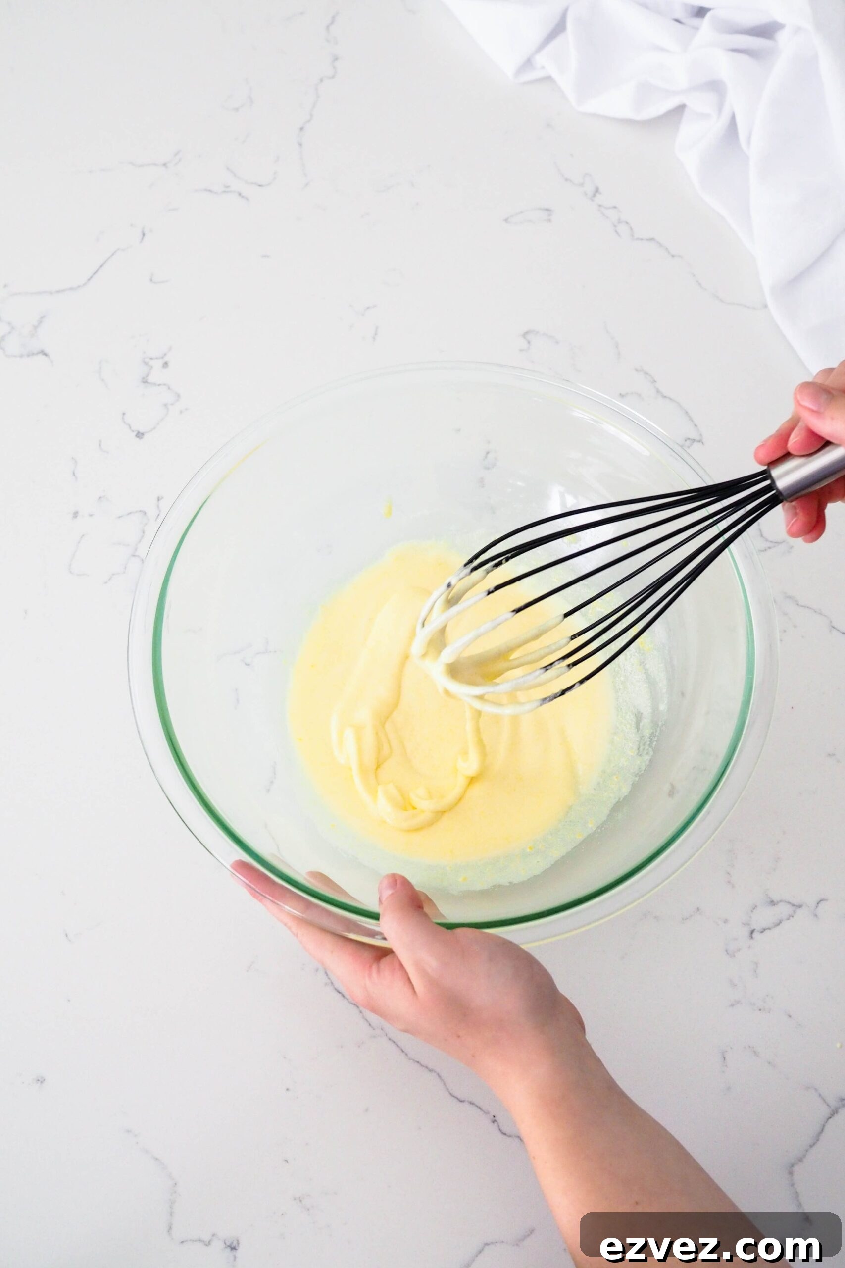 A ribbon of beaten eggs and sugar flows off a whisk in a bowl.