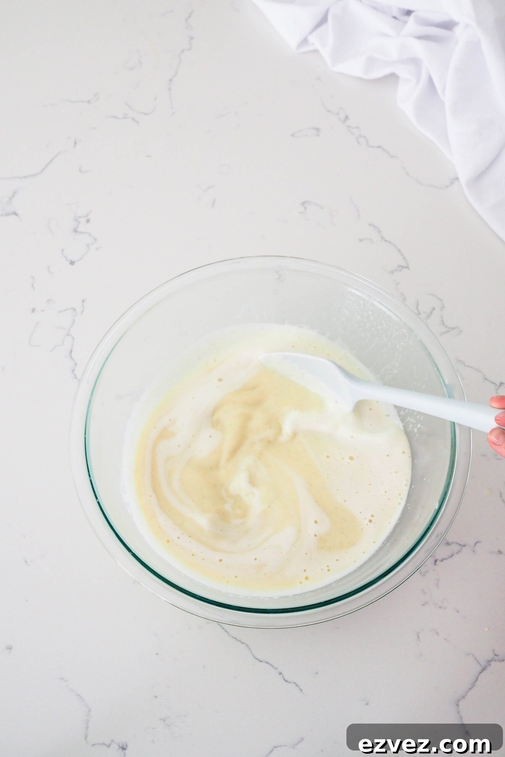 A spatula stirs vanilla bean paste into custard.