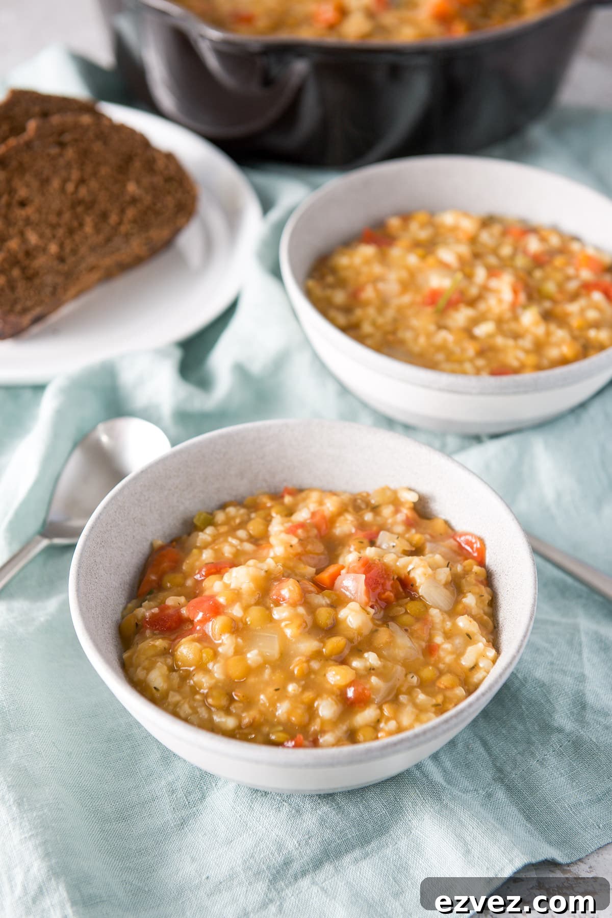 Two grey bowls filled with the thick soup with some bread and the pan behind them