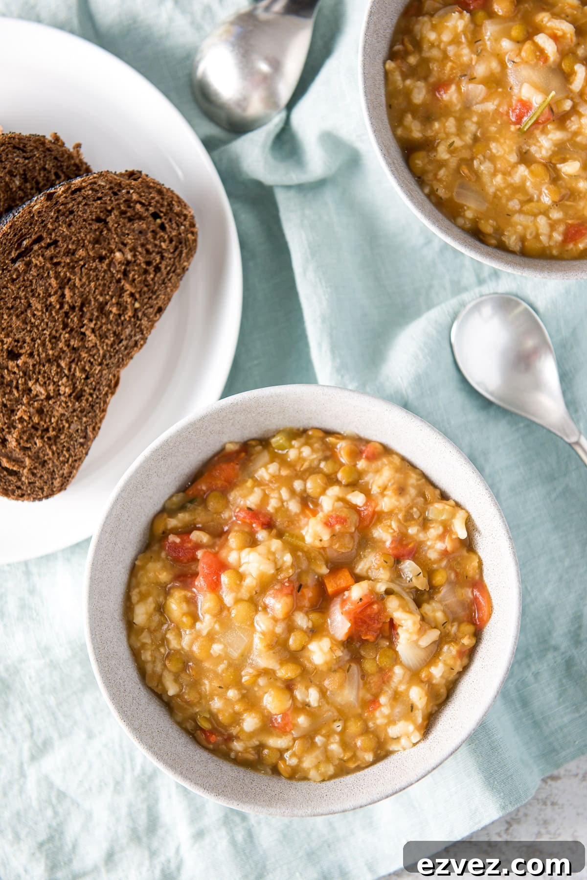 Overhead view of the bowls with the thick chunky soup with a white plate of dark bread
