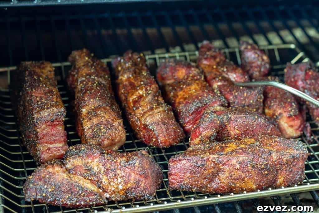 multiple strips of boneless country style ribs with rub in a smoker, one strip has a temp probe in it