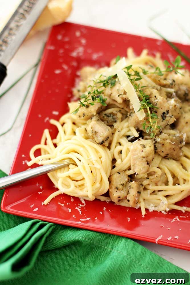 Red plate containing Garlic Basil Chicken Pasta topped with shaved Parmesan cheese and thyme, fork spiraling noodles. 