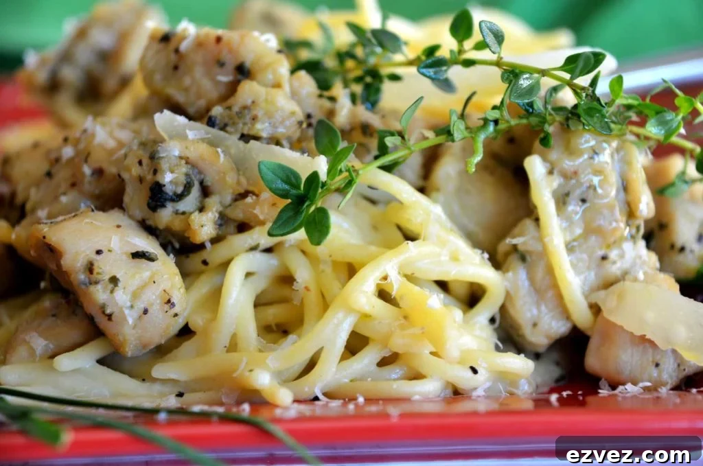 Red plate containing Garlic Basil Chicken Pasta topped with sprigs of fresh thyme and Parmesan cheese on top of cooked spaghetti noodles.
