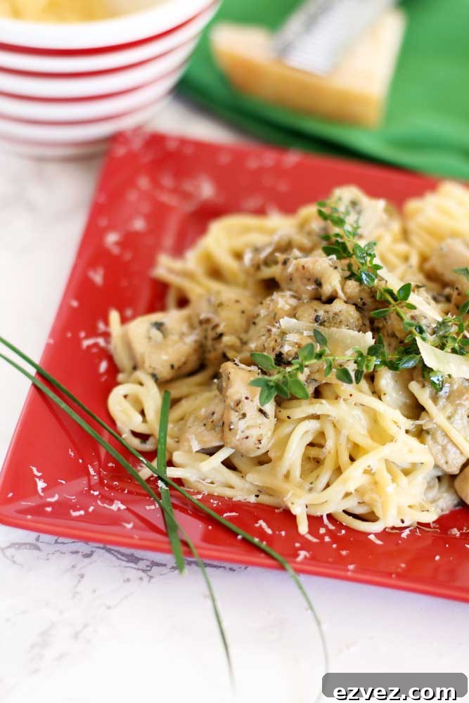 Red plate containing Garlic Basil Chicken Pasta topped with fresh sprigs of thyme and Parmesan cheese sitting on a white marble table.