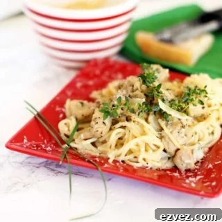 Red plate containing Garlic Basil Chicken Pasta topped with fresh thyme and Parmesan cheese.