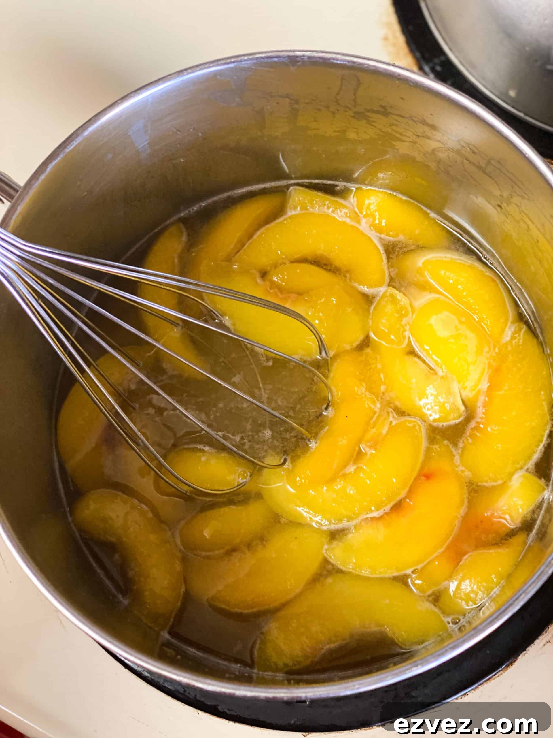 Peaches in sugar water being stirred with a whisk
