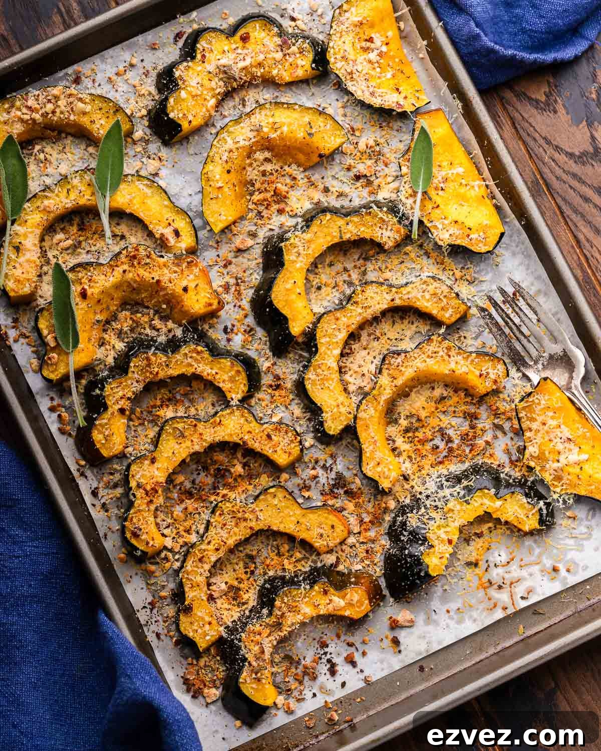 Parmesan roasted acorn squash on baking sheet with fork and blue napkin.