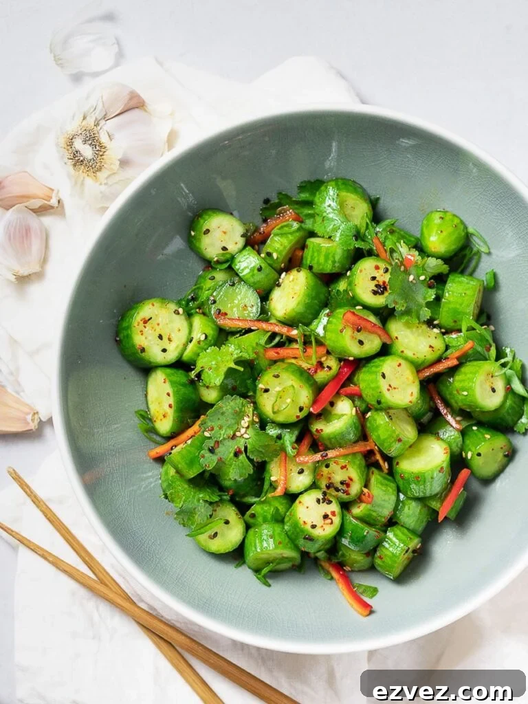Spicy Asian cucumber salad with herbs and red pepper in a blue bowl next to garlic and chopsticks