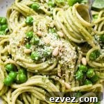 Pesto pasta made with spaghetti in a speckled ceramic bowl with a fork twirling a bite, topped with pine nuts and grated parmesan.