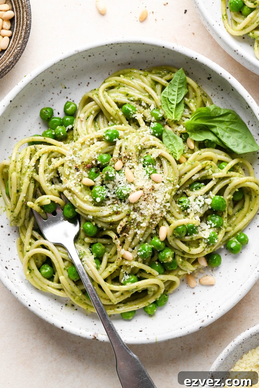 Pesto pasta made with spaghetti twirled in a speckled ceramic bowl and topped with pine nuts and grated parmesan.