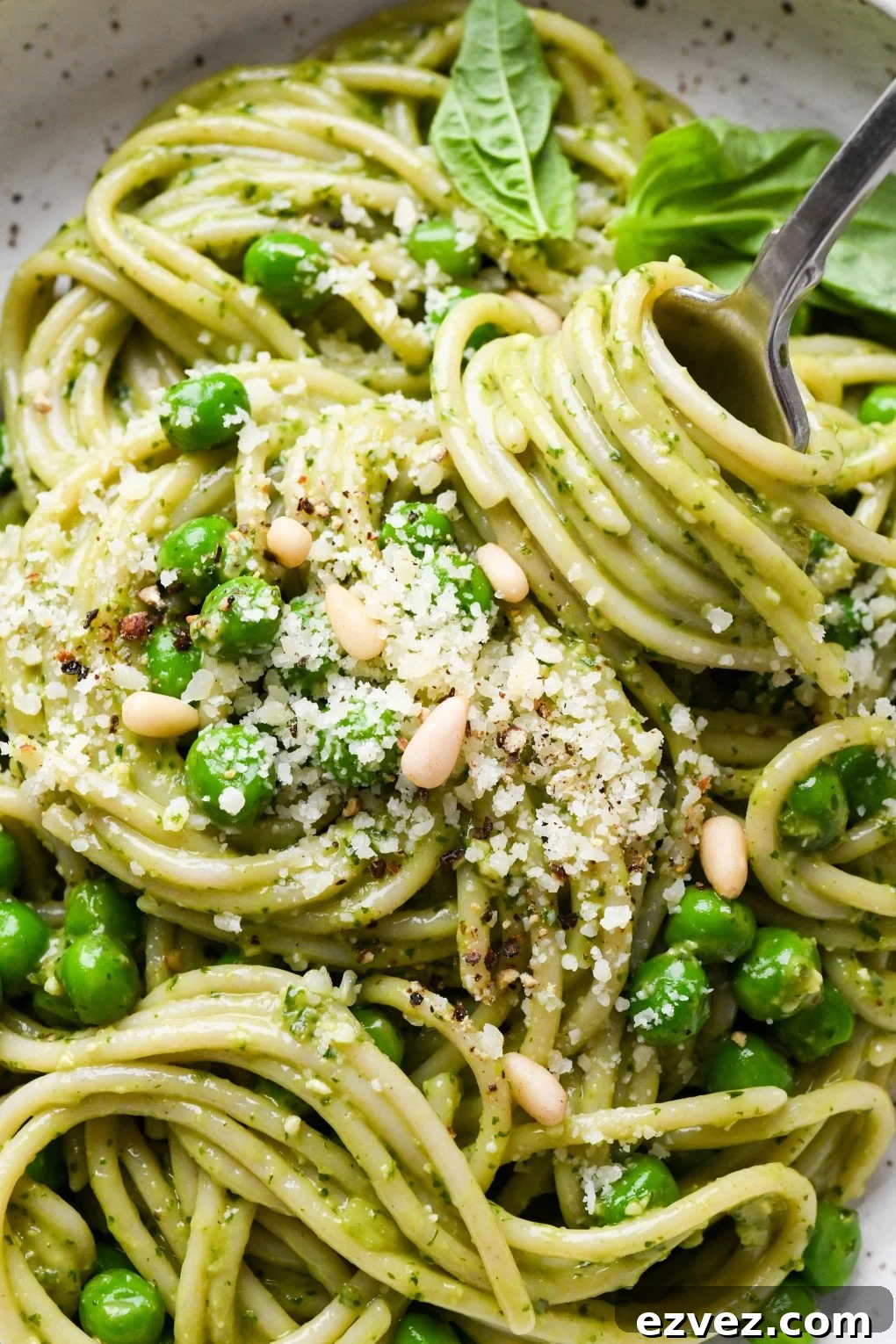 Pesto pasta made with spaghetti in a speckled ceramic bowl with a fork twirling a bite, topped with pine nuts and grated parmesan.