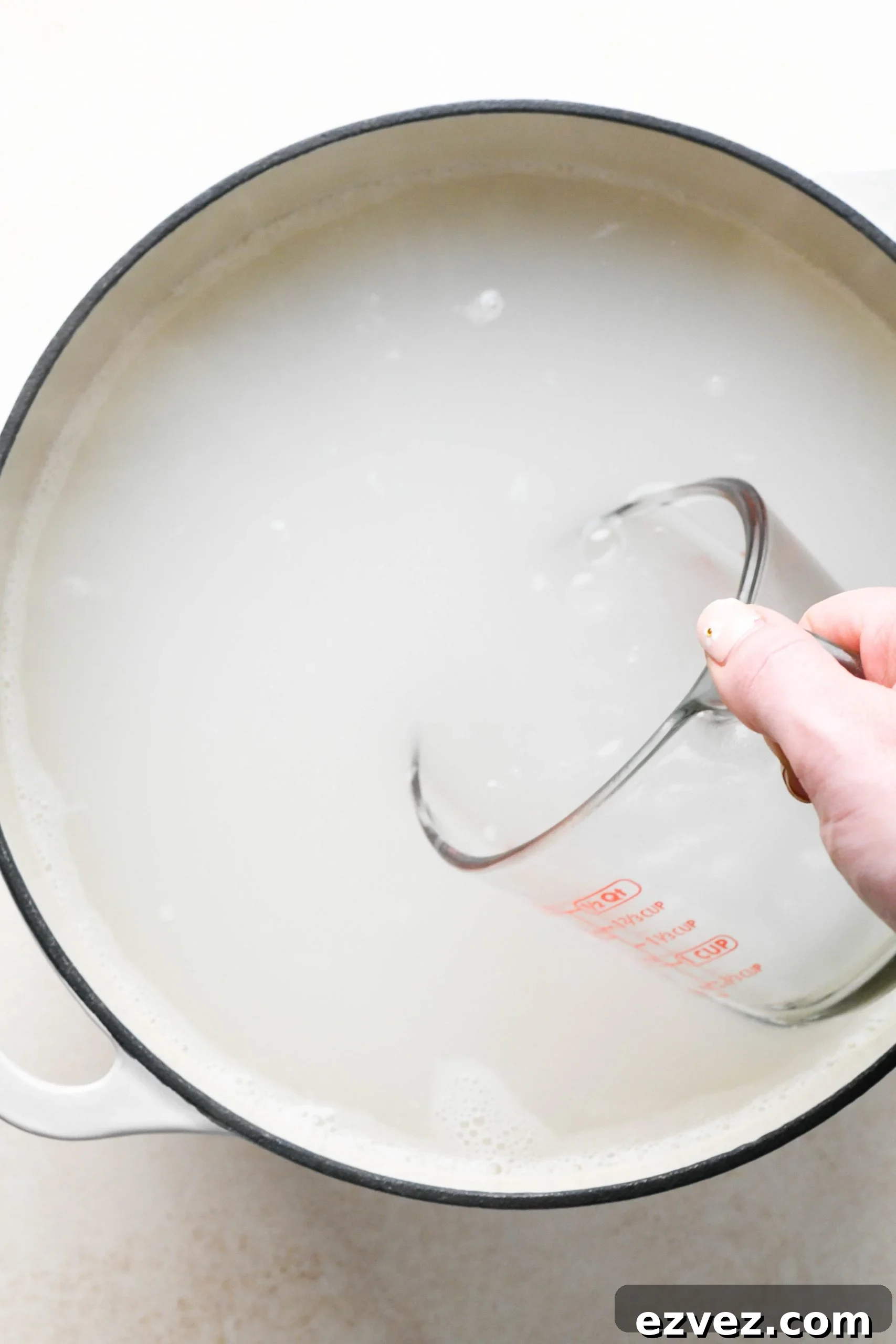 How to make easy pesto pasta: A hand dipping a glass measuring cup into pasta water.