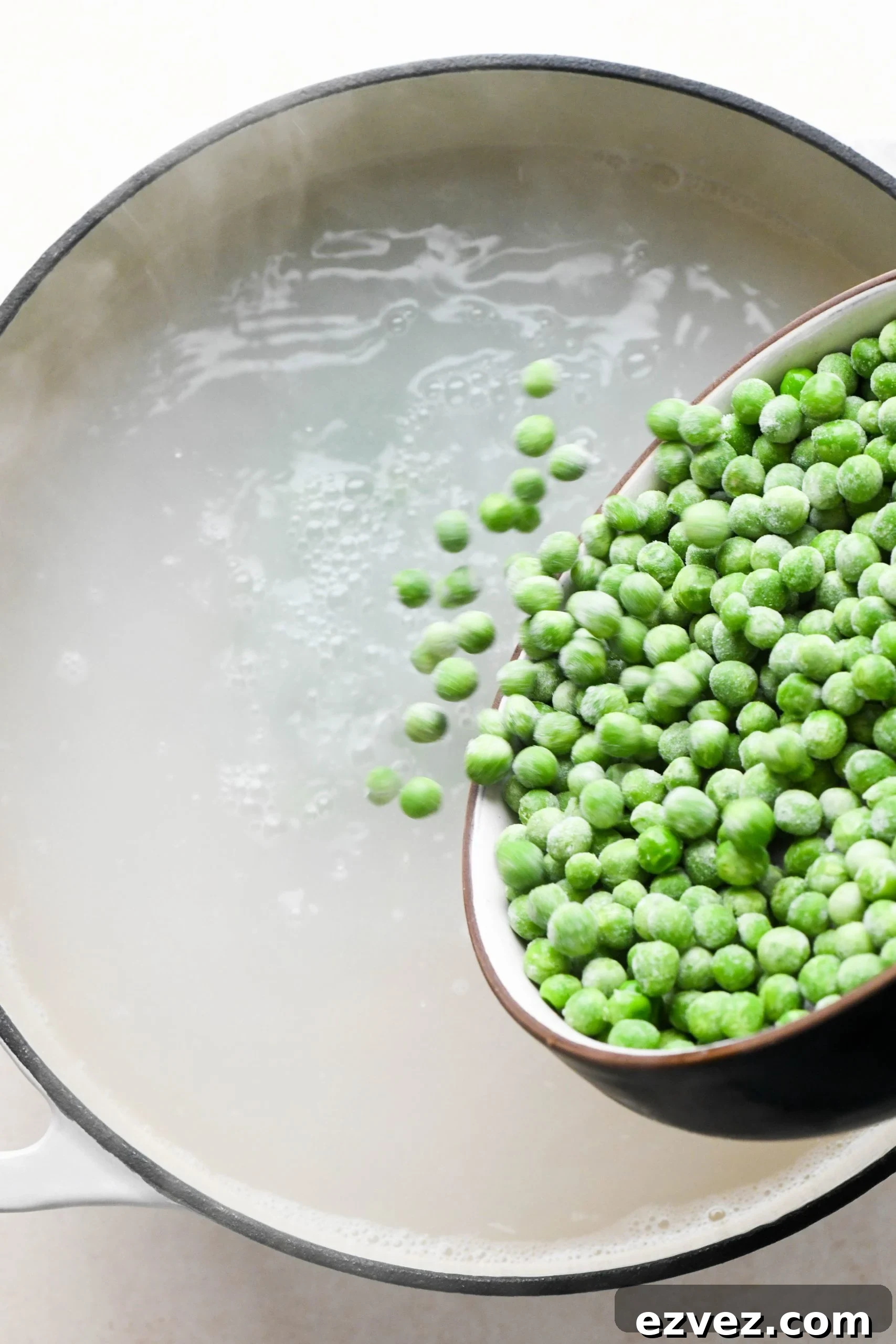 How to make easy pesto pasta: Pouring frozen peas into boiling pasta water.