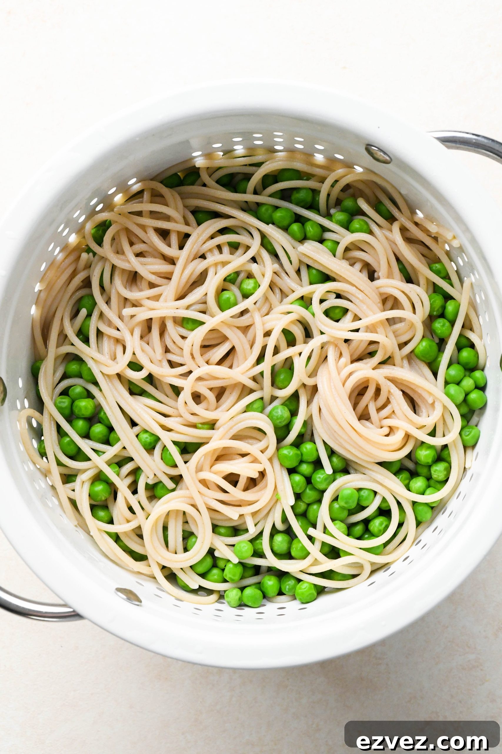How to make easy pesto pasta: Cooked spaghetti and peas in a strainer.