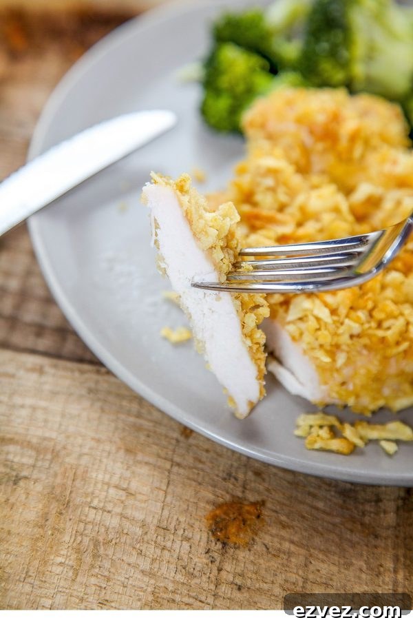 a fork holding a bite of chicken coated in potato chips. 