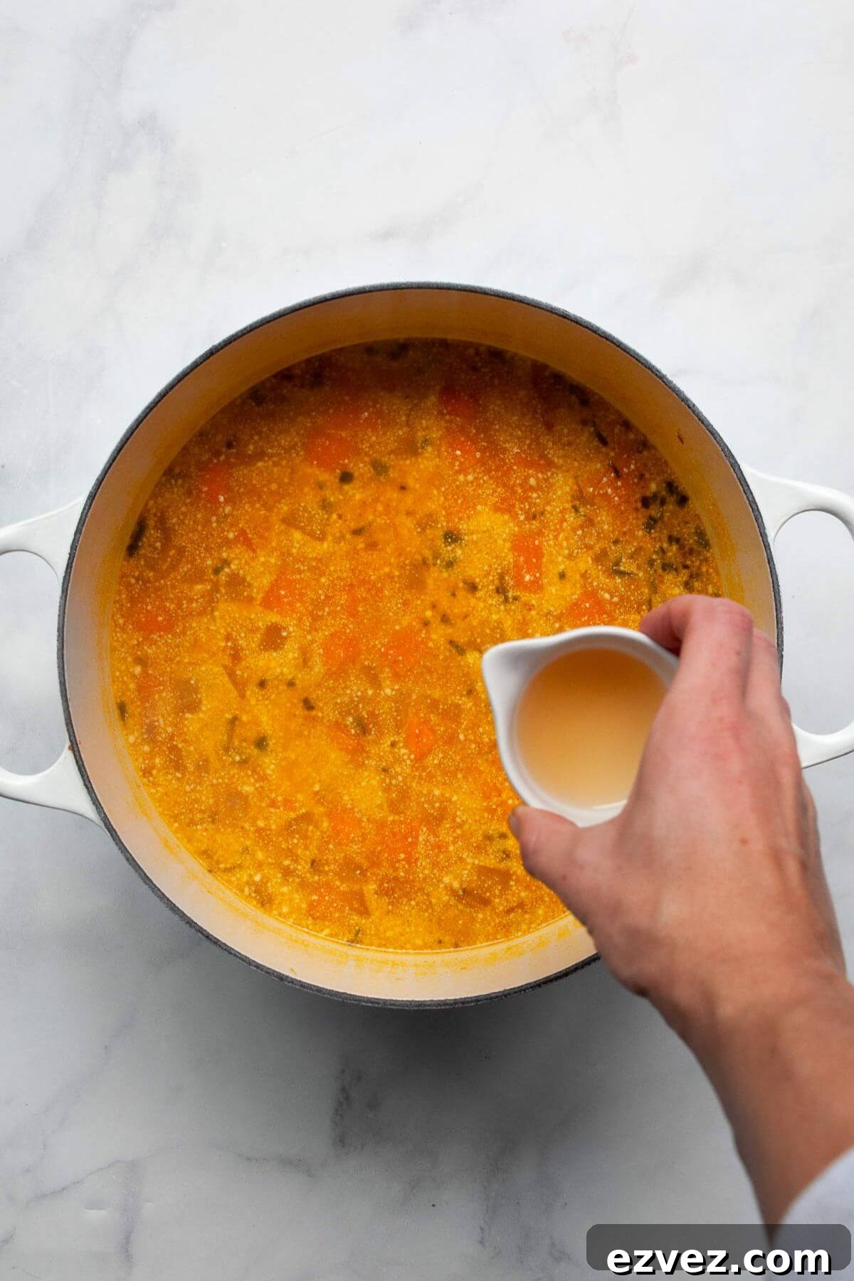 Pouring apple cider vinegar into simmering sweet potato and pumpkin soup.