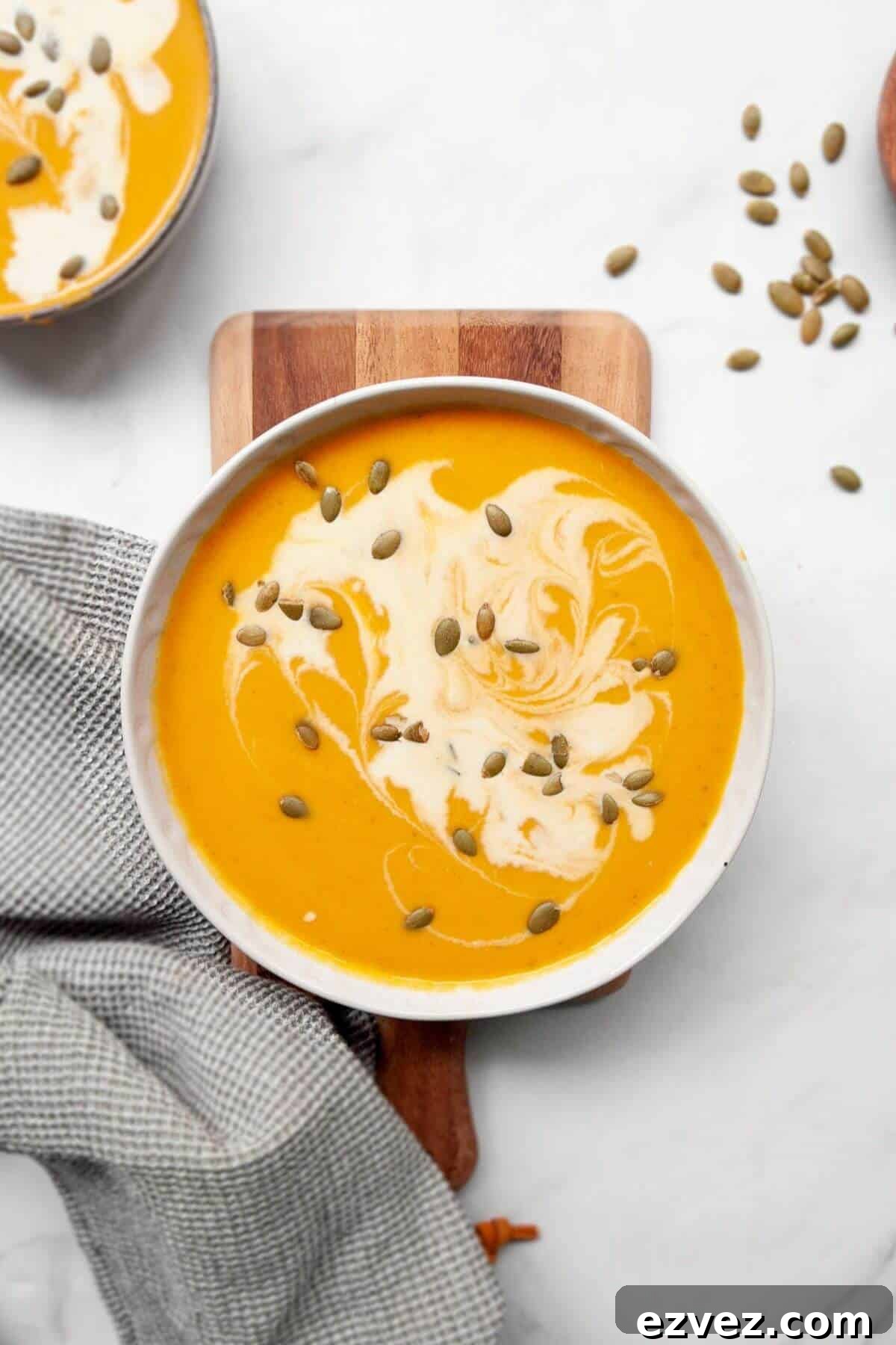 Silky smooth pumpkin and sweet potato soup in a bowl with pumpkin seeds and coconut milk on top.