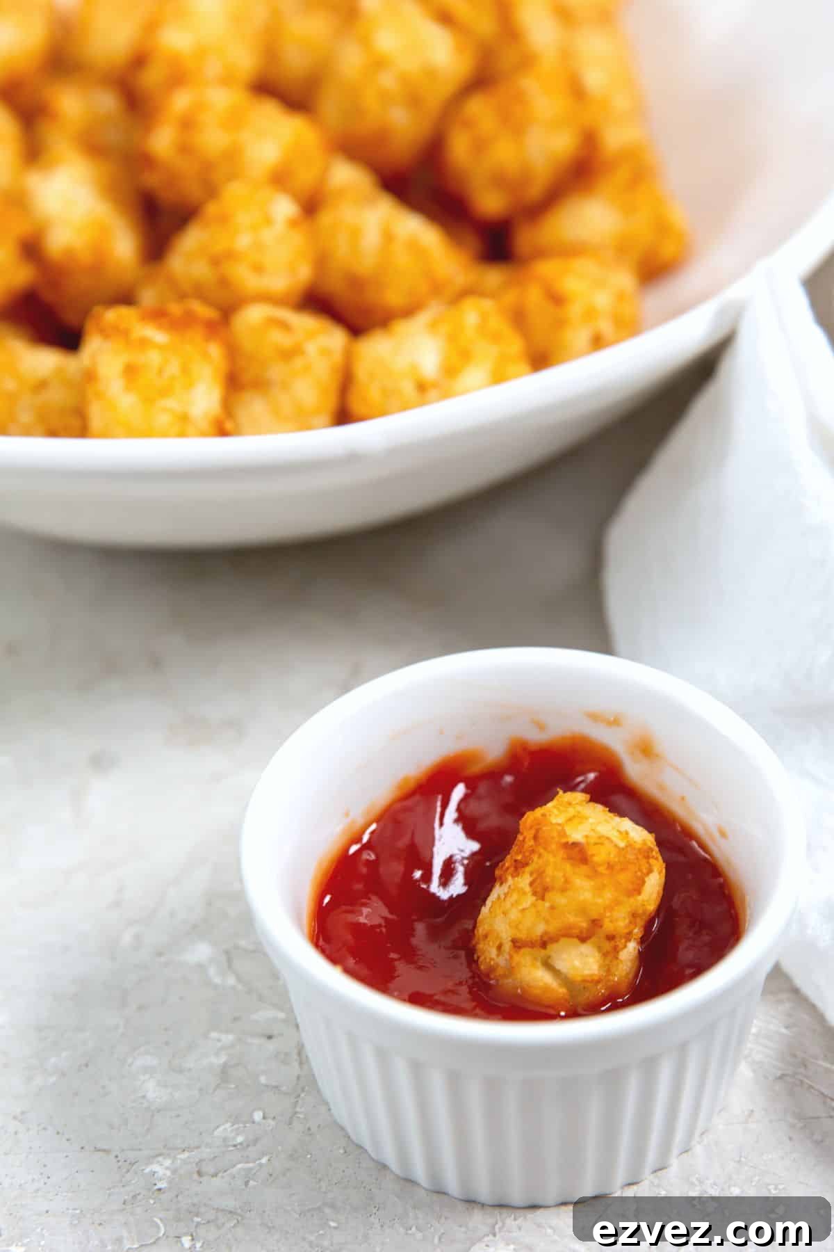 A small ramekin with ketchup and a tater tot.