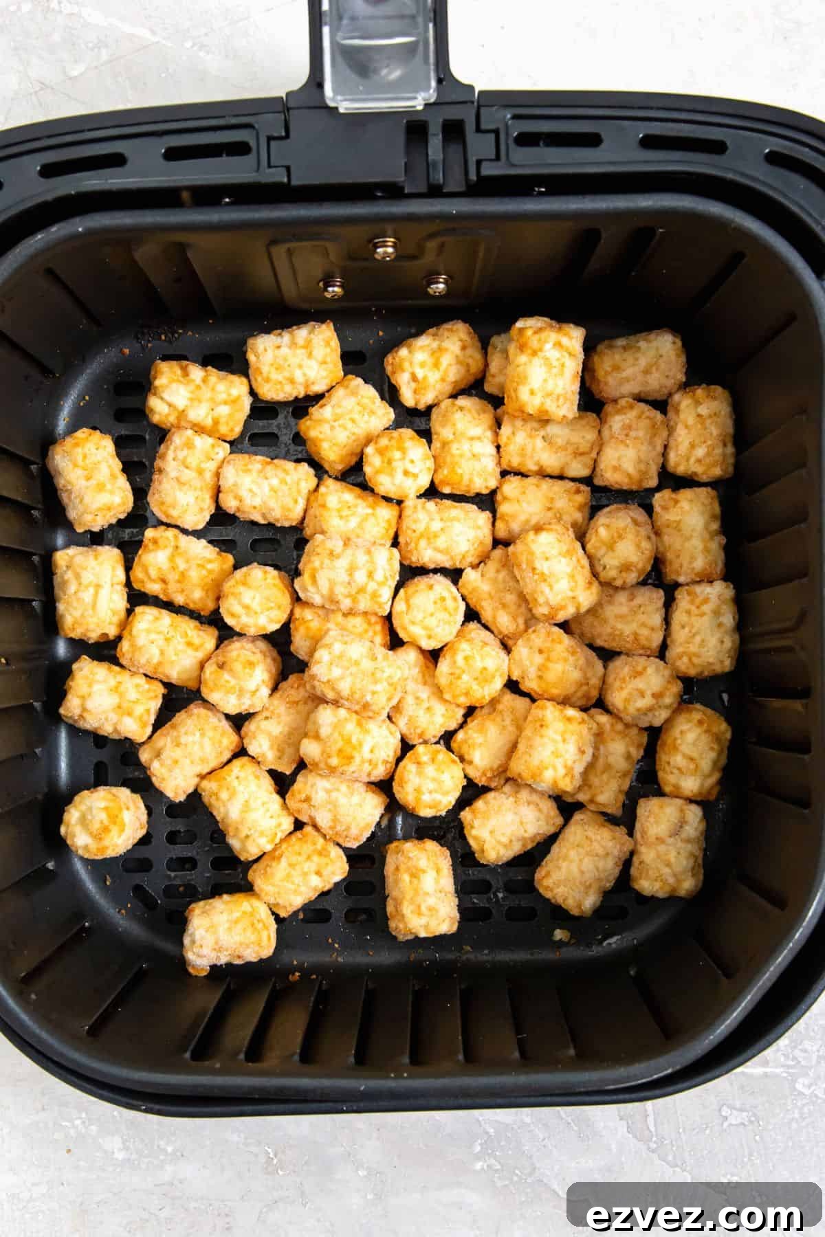 Frozen tater tots in an air fryer basket.