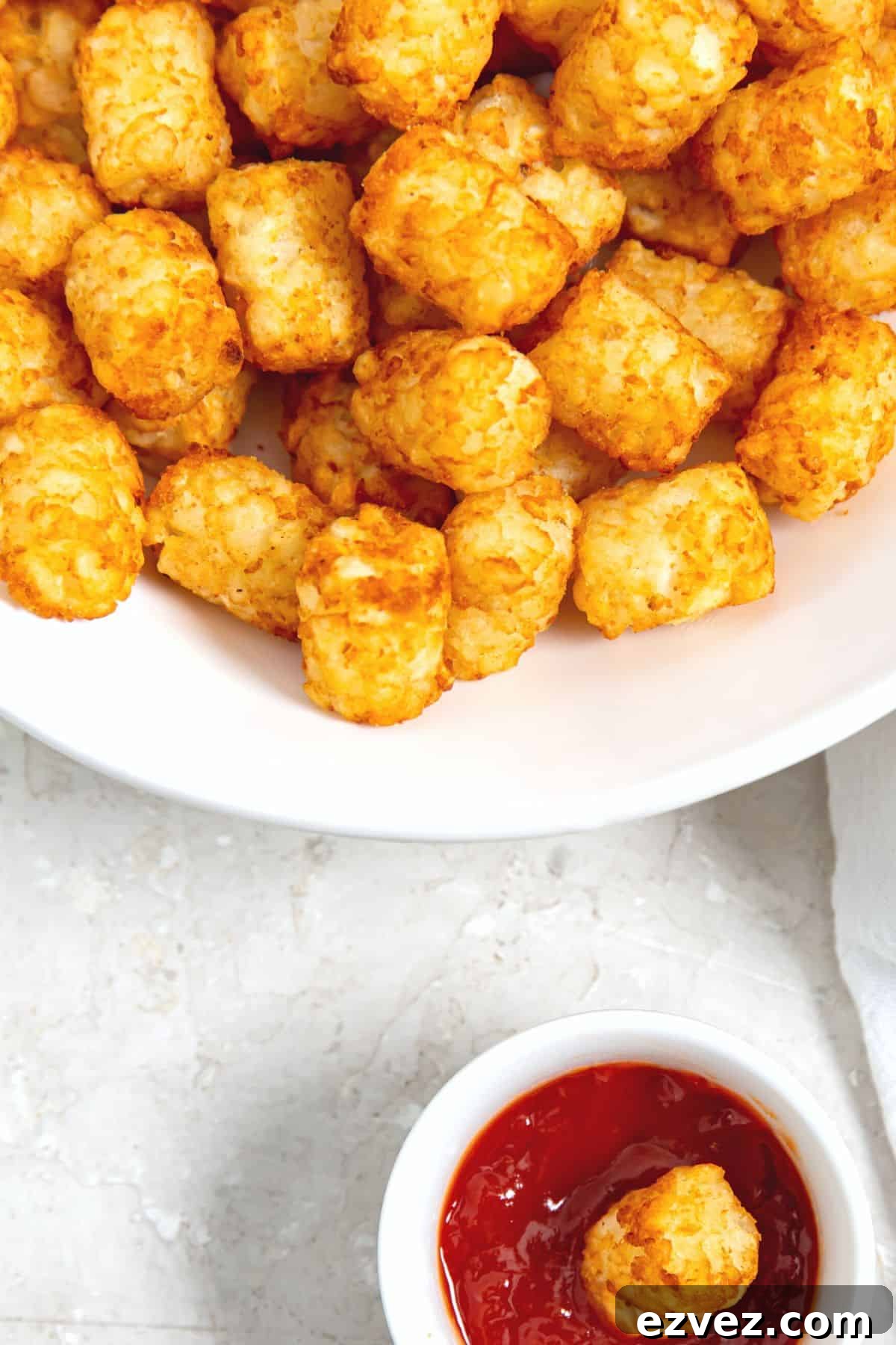Top down view of a bowl of air fried tater tots and a small ramekin with ketchup.
