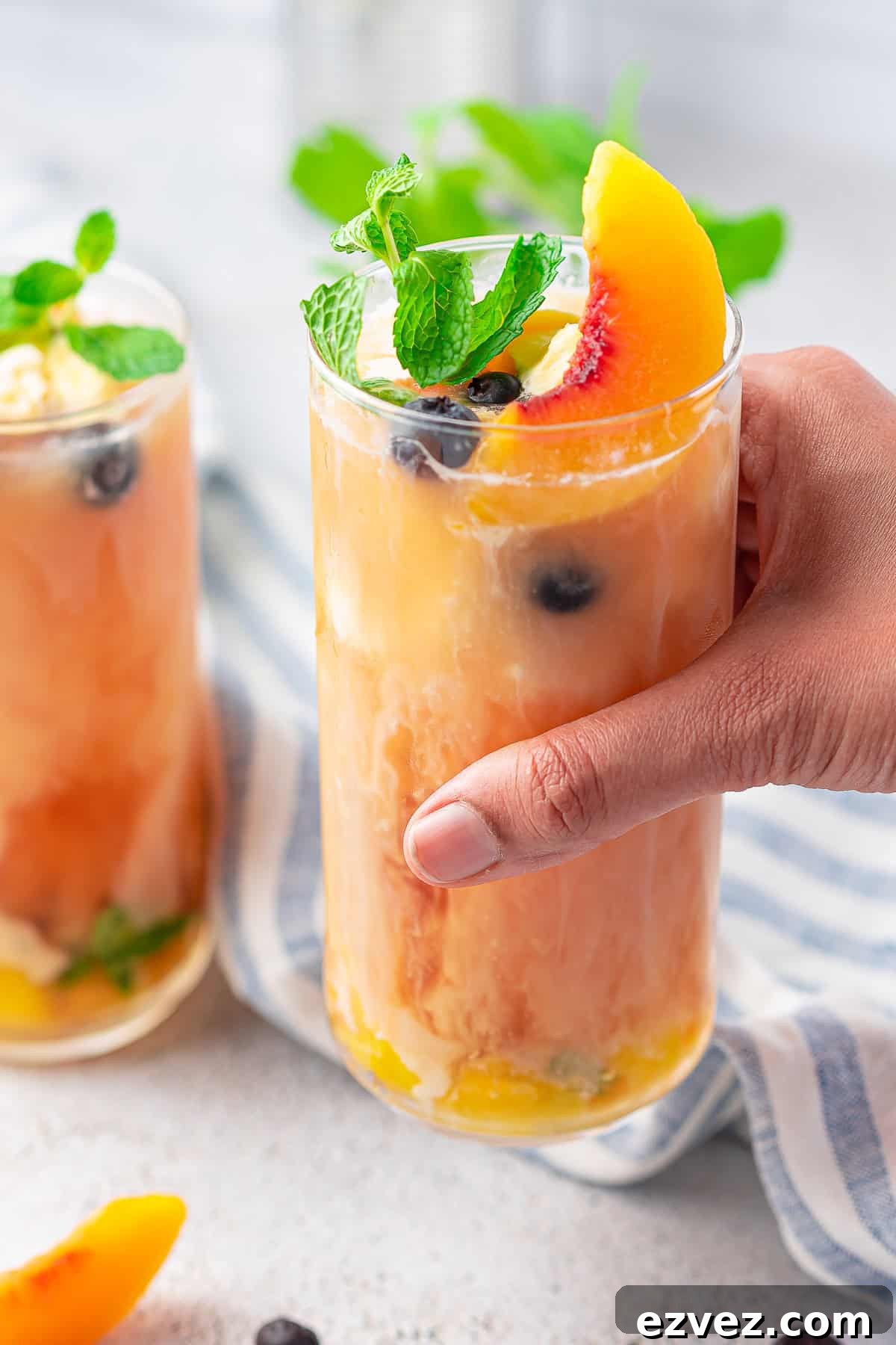 Creamy Peach Iced Tea Recipe: Smooth, Refreshing Summer Drink 7 Hand holding up a glass of tea showing off the melted ice cream and garnishes.