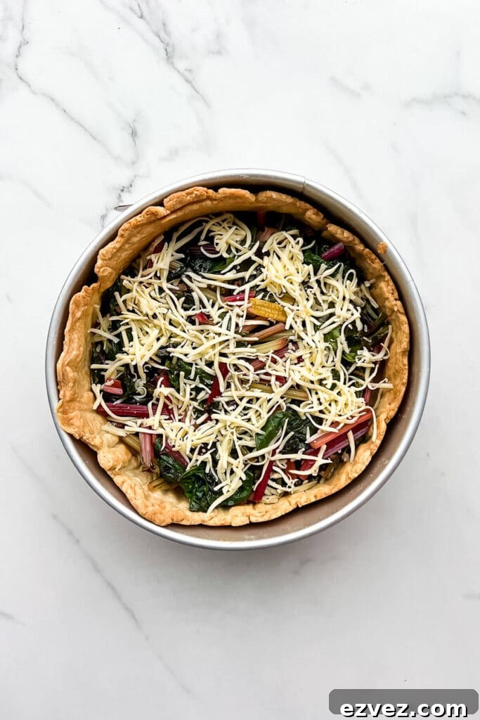 Layering sautéed rainbow Swiss chard and cheese in a blind-baked crust to make a quiche.